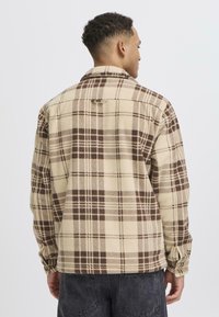 Beige and brown checkered flannel jacket with a collared neckline, button cuffs, and a hanging loop detail on the back. Soft texture.