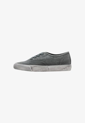 Sneaker in tela grigia a taglio basso con lacci e suola in gomma bianca usurata, mostrata di lato su sfondo bianco.