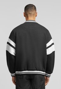 Black sweatshirt with white stripes on sleeves, ribbed cuffs, and collar. Soft fabric with a relaxed fit and elastic waistband.
