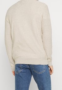 Beige Strickpullover mit Rundhalsausschnitt und langen Ärmeln, mit lockerem Schnitt und gerippten Bündchen, kombiniert mit blauen Jeans.