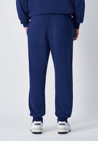 Dunkelblaue Sporthose mit entspannter Passform, elastischem Bund und Bündchen. Dazu weiße Sneakers mit navy- und schwarzen Akzenten.