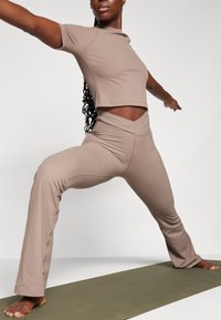 Ensemble de vêtements de sport taupe à côtes comprenant un haut court et un pantalon évasé. Le haut a des manches courtes ; le pantalon présente une taille large et pliée.