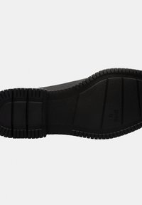 Suola di sneaker in gomma nera con una superficie testurizzata, caratterizzata da profondi modelli di battistrada e bordi scanalati per una migliore aderenza. Include una costruzione flessibile e solida.