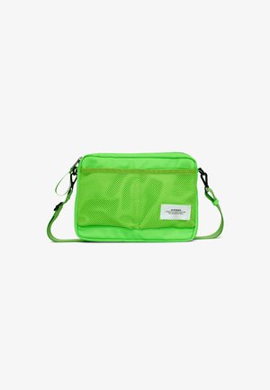 Neon grøn skuldertaske med front i mesh, lynlåsåbning og justerbar rem. Har et mærke nederst til højre til branding.