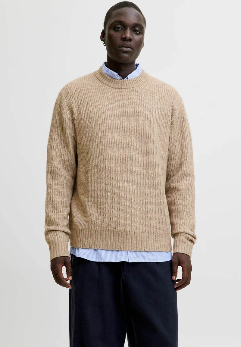 Beige ribbed knit sweater with a crew neckline, paired with a light blue button-up shirt underneath. Wool-like texture, relaxed fit.