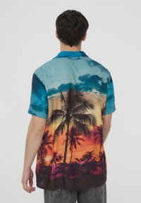 Camicia con bottoni in tessuto liscio caratterizzata da un tramonto sfumato con palme. Le transizioni di colore vanno dal blu all'arancione e al viola. Maniche corte.