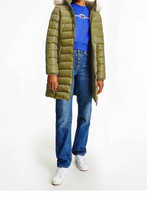 Manteau matelassé vert olive avec une capuche en fourrure, porté sur un pull bleu et un jean bleu taille haute. Des baskets blanches complètent le look.