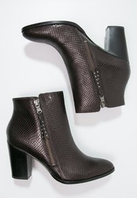 Stivali alla caviglia in similpelle di serpente marrone con tacco spesso, cerniera laterale e borchie decorative lungo la linea della cerniera. Finitura liscia e testurizzata.