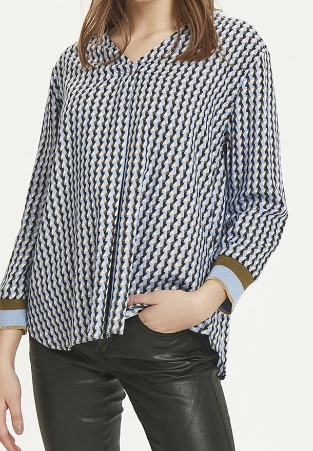 Kvinna som bär en långärmad mönstrad blus med blå, vita och bruna geometriska former, tillsammans med svarta läderbyxor.