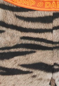 Shorts med tigertryck som har en texturerad, pälsliknande yta. Den orange midjan pryds av texten "#DUMP". I huvudsak beige med svarta ränder.