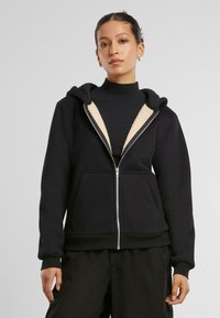 Felpa nera con zip, foderata in morbido pile beige, dotata di cappuccio e ampie tasche frontali. Tessuto morbido e maniche con polsini. Vestibilità comoda.