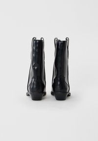 Stivali alla caviglia in pelle nera con una texture liscia, tacco basso e dettagli di cucitura minimi. Il retro presenta delle linguette per un facile indossamento.