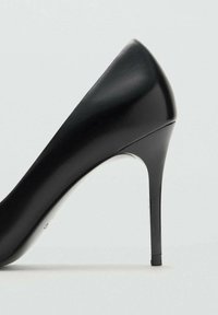 Zapato de tacón alto negro con acabado de cuero suave, puntera afilada y tacón stilettos delgado. Diseño simple sin acentos notables.