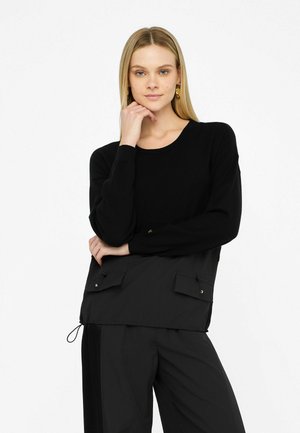 Maglione nero con maniche lunghe, scollo rotondo e due tasche frontali. Realizzato in un tessuto morbido con una vestibilità rilassata e dettagli di cucitura sottili.