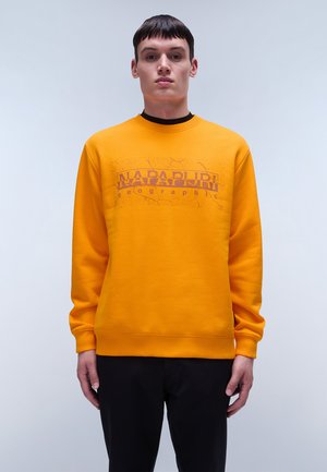 Geel sweatshirt met ribgebreide boorden en halslijn. Beschikt over een grafische print in donkerdere tinten, geplaatst aan de voorkant in het midden. Zwarte broek.