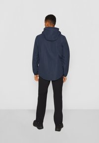 Veste imperméable bleu marine avec capuche, en matériau léger, manches longues et ourlet arrondi, associée à un pantalon noir et des bottes.