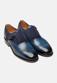 Marineblaue Lederschuhe mit Broguemuster, einer glatten Oberfläche und einem Wildlederriemen mit einer Schnalle. Runde Zehen und kontrastierende Texturen.