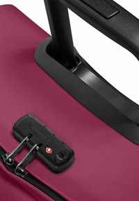 Mörk röd hård resväska med en texturerad yta, utrustad med ett svart utdragbart handtag, dragkedja och ett säkerhetslås.