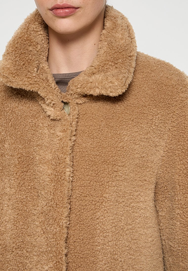 Veste en polaire marron au toucher pelucheux, avec un col et une fermeture à un bouton unique. Aucun motif ni quincaillerie visibles.