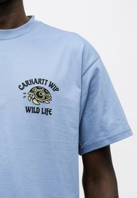 Γαλάζιο κοντομάνικο μπλουζάκι με μικρό σχέδιο χελώνας και κείμενο "Carhartt WIP Wild Life" στο αριστερό στήθος.