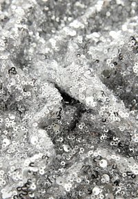 Tessuto argentato con paillettes, caratterizzato da una superficie testurizzata con paillettes rotonde sovrapposte di diverse dimensioni, che riflettono la luce in molteplici direzioni.