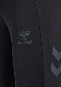 Leggings deportivos negros hechos de un tejido elástico, con un logo sutil y un patrón de chevron en gris oscuro a lo largo del costado.