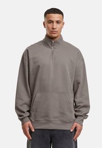 Sweatshirt gris à demi-fermeture éclair fabriqué en tissu doux, doté d'un col haut, d'une poche avant, et d'une coupe décontractée avec des poignets et un ourlet côtelés.