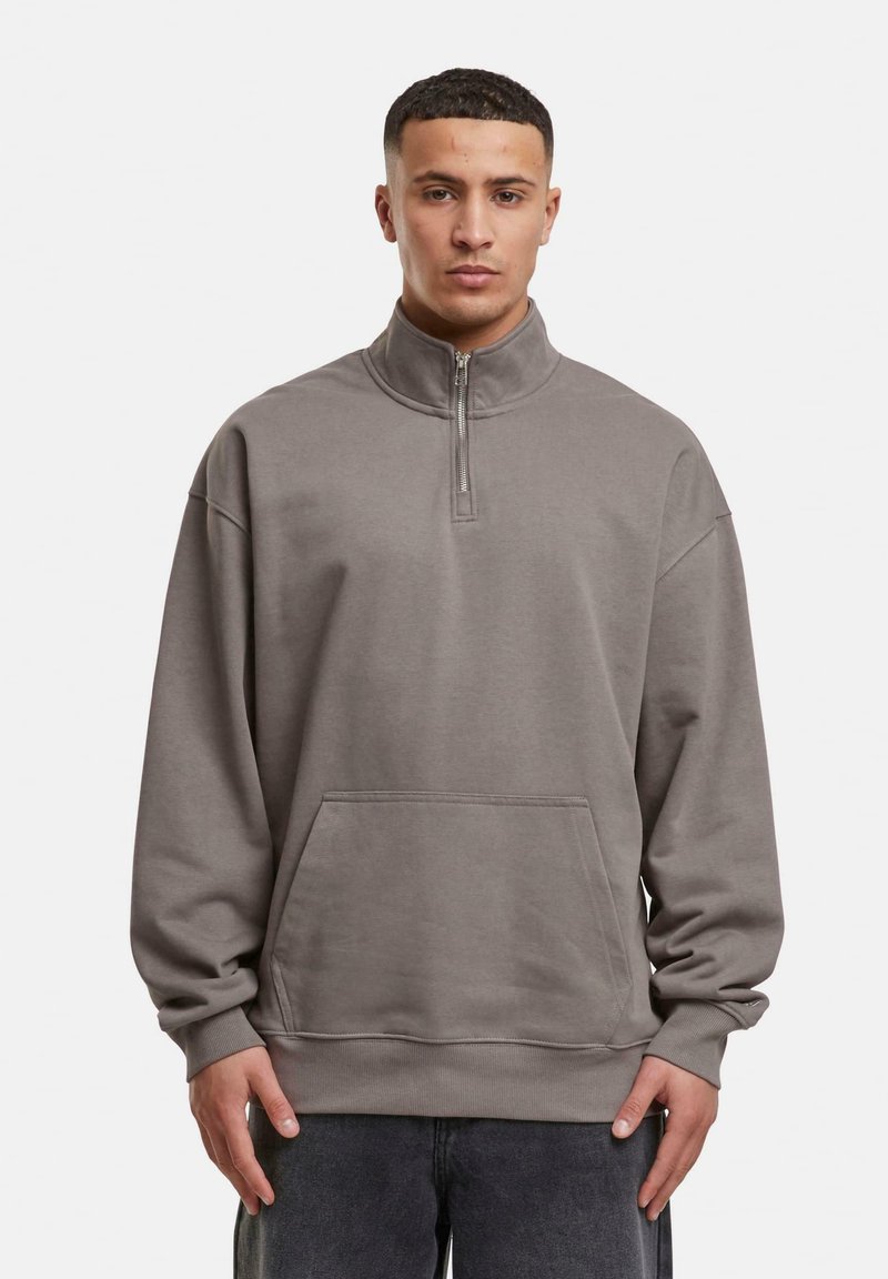 Sweatshirt gris à demi-fermeture éclair fabriqué en tissu doux, doté d'un col haut, d'une poche avant, et d'une coupe décontractée avec des poignets et un ourlet côtelés.