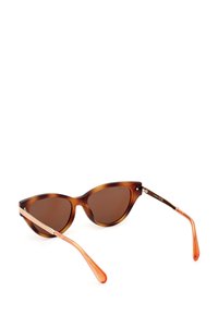 Gafas de sol estilo ojo de gato en carey, con lentes tintados marrones, patillas con detalles en naranja y acabados metálicos en las varillas.