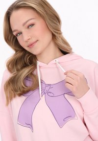 Sudadera rosa con un gran gráfico de moño púrpura y cordones blancos. Tejido suave con un ajuste relajado y puños acanalados.