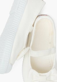 Zapatos de tela blancos con un diseño plano, que presentan un detalle de lazo en la parte delantera y una suela de goma texturada para un mejor agarre.