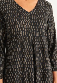 Haut à col en V en tissu doux avec un motif abstrait noir et beige. Dispose de manches trois-quarts et d'une coupe décontractée.