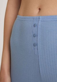 Blauwe geribde broek van een gestructureerde stof, met drie knopen langs de tailleband en een gladde afwerking, van dichtbij bekeken.