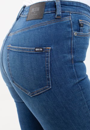 Pantalones vaqueros de mezclilla azul con un diseño ajustado, que cuentan con costuras naranjas, una etiqueta de cuero en la cinturilla y un bolsillo trasero con una etiqueta de la marca.