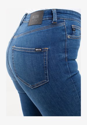 Jeans in denim blu con un design aderente, caratterizzati da cuciture arancioni, un'etichetta in pelle sulla vita e una tasca posteriore con un'etichetta del marchio.
