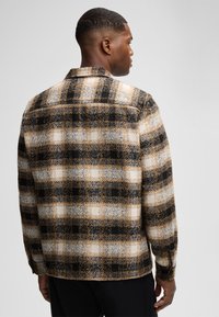 Camicia a quadri in flanella nera, bianca e beige, con una vestibilità rilassata, tasca con bottone e tessuto strutturato. Vista posteriore mostrata.