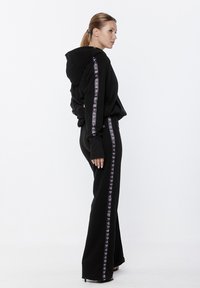 Czarna, kapturowa bluza i dopasowane spodnie, wykonane z miękkiego materiału. Ozdobne paski z powtarzającym się wzorem logo biegną wzdłuż boków.