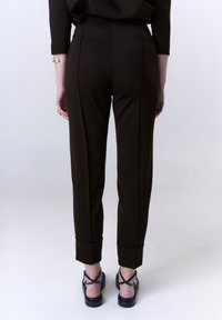 Bruine op maat gemaakte broeken met een slim fit, voorzien van een achterzak en opgerolde pijpen. Gepaard met zwarte sandalen met bandjes.