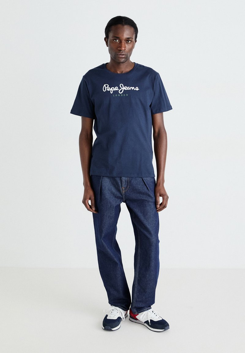 Navyblaues Baumwoll-T-Shirt mit weißem "Pepe Jeans London"-Logo. Kombiniert mit blauen Jeans und schwarz-weißen Sneakers.
