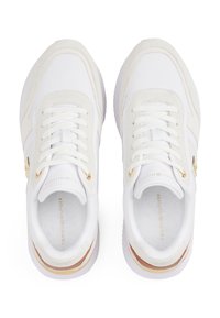 White sneakers with suede and mesh panels, flat laces, gold accents, and a thick sole. Minimalist design with a logo on the insole.
