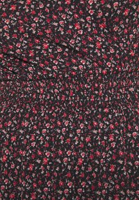 Schwarzer Stoff mit einem floralen Muster in roten und rosa Farbtönen. Verfügt über ein smockiertes Design mit kleinen Blumen, die gleichmäßig verteilt sind.