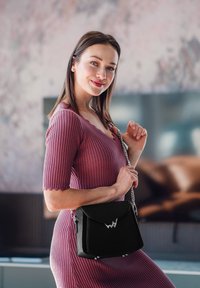 Černá strukturovaná kabelka se stříbrným řetízkovým popruhem a logem. Kabelka má překládaný klapkový uzávěr a texturovaný povrch, což dokonale doplňuje žebrované šaty.