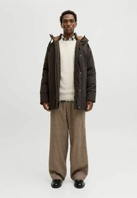 Pufjakas tumši brūnā krāsā ar vilnas oderi apkaklītē. Krēmveida džemperis un rakstainā krekla apakšā, apvienots ar platām brūnā krāsā biksēm. Melni apavi.