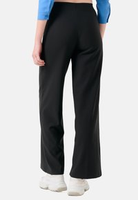 Pantalons larges noirs avec un drapé modéré, une texture lisse et une finition soignée, associés à des chaussures de sport blanches.