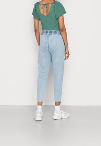 Grön randig topp med korta puffärmar och detalj med knytning i ryggen; ljusblå denimjoggers med elastisk midja; vita sneakers.