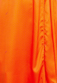 Tissu orange vif avec de petits motifs en losange violets, présentant une texture lisse et des détails de plissage sur un côté.