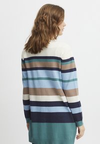 Lielizmēra svītrainais džemperis, kas veidots no tumši zilas, tirkīza, brūnas un krēmkrāsas, ar mīkstu tekstūru un ribinātu apakšmalu.