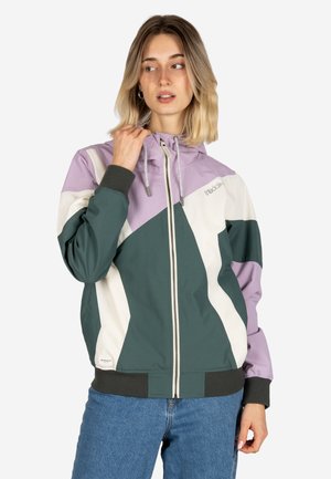 Woman wearing a zip-up hooded jacket with green, white, and lavender color blocks, paired with blue jeans, posing with hand near collar.