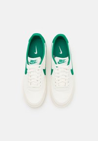 Valged nahast spordijalatsid roheliste detailidega, millel on pehme kaelus, valged paelad ja tekstureeritud tald. Nike logo keelega ja külgedel.