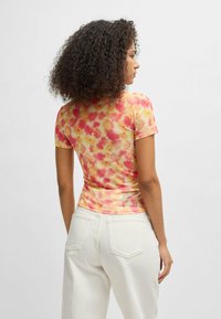 Short-sleeve, fitted floral top in soft, stretchy fabric featuring a pattern of pink and orange flowers on a yellow background.
